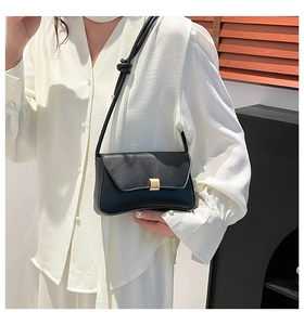 Close-up of minimalist black leather baguette bag featuring a gold buckle and knotted strap