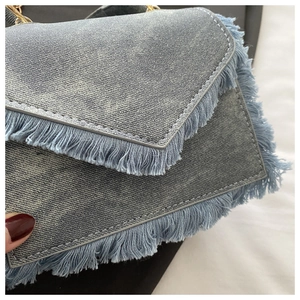 Detail of denim fabric texture with fringe edges and golden metal chain on a small square bag