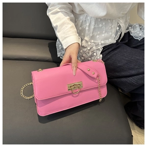 Detail of a bright pink crossbody bag with a gold D-ring buckle on a leather sofa