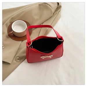 Detail of red glossy leather handbag featuring a decorative gold bow buckle and top handle