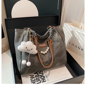 Detail of grey tote bag with brown leather handles, silver chain, and pearl pendant decor