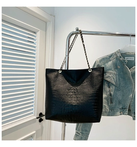 Detail of black crocodile embossed tote bag with elegant gold and black chain strap
