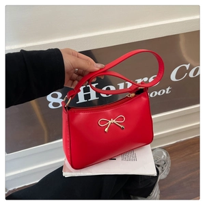 Detail of red leather underarm bag with elegant gold metal bow and zipper closure