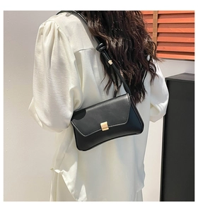 Detail of minimalist black leather baguette bag with a square gold metallic buckle