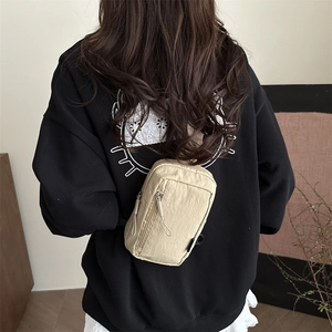 Minimalist beige nylon chest bag with two zipper compartments shown on a model