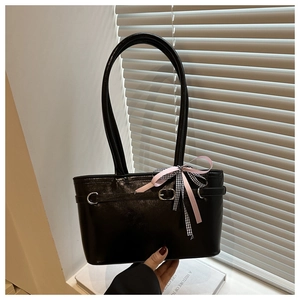 Détail d'un sac à bandoulière noir brillant avec boucle en métal et nœud rose