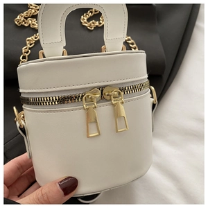 Detailansicht der weißen Leder-Zylindertasche mit goldenem Reißverschluss und Kettenriemen
