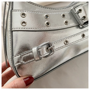 Detail of silver metallic Y2K shoulder bag with grommet buckles and punk rivets texture