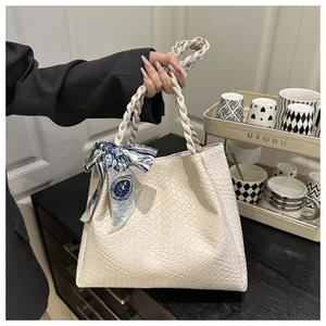 Detailed view of beige woven tote bag with decorative blue silk scarf and dual handles