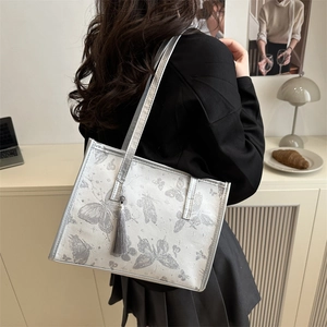 Silver tote bag with butterfly print and tassel charm worn by model in minimalist setting