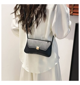 Detail of a black leather shoulder bag with a gold rectangular metal buckle on a model
