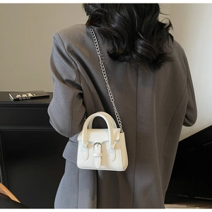 Detail of white mini leather crossbody bag with silver chain strap on a blazer outfit