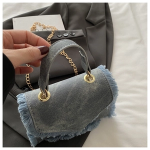 Close-up of denim crossbody bag featuring frayed fringe edges and gold chain strap