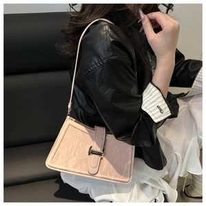 Detail of pink marble-textured shoulder bag with a gold H-shaped buckle on a model