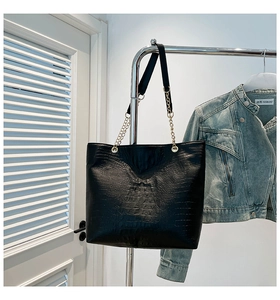 Detail of black crocodile embossed tote bag featuring gold chain strap and glossy texture