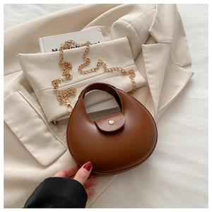 Brown leather crescent bag detail with golden chain strap and magnetic snap closure