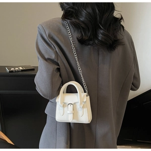 Back view of a mini white leather square handbag with silver chain on a gray suit