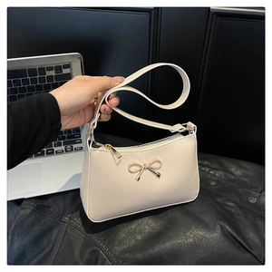 Close-up of beige PU leather shoulder bag with a gold bow accent and zip closure