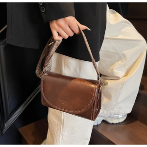 Detail of vintage brown leather bag with wide jacquard strap and embossed fashion logo
