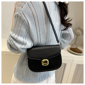 Détail d'un sac besace en cuir noir mat porté par un mannequin dans un décor chaleureux