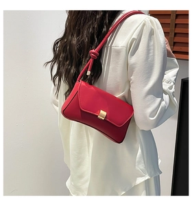 Detail of red leather shoulder bag showing the golden metal buckle and knot strap detail