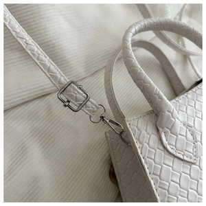 Close-up of white woven bag featuring cylindrical handle and silver metal hardware details