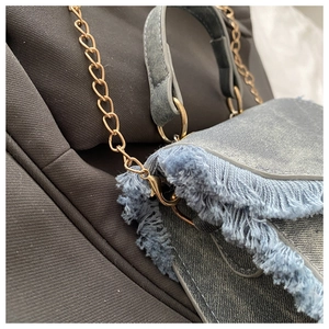 Detailed shot of frayed denim fabric texture and gold chain on light blue crossbody bag