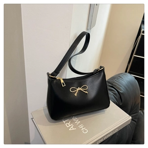 Detail showing sleek black shoulder bag with elegant gold bow metal accessory
