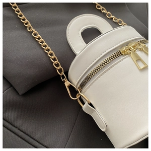 Detail der weißen Mini-Eimertasche mit Goldkette und Tragegriff auf grauem Stoff