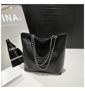 Close-up of black faux leather tote bag with crocodile texture and gold chain straps
