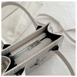 Detail of woven texture, silver star emblem and zipper closure on cream crossbody bag