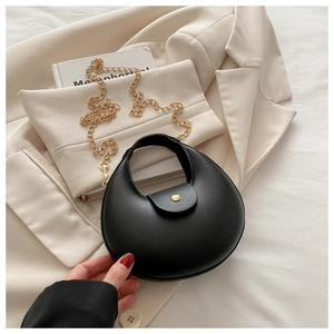 Detail of minimalist black crescent bag featuring gold stud magnetic closure and chain