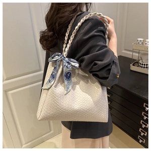 Detail of white woven tote bag with a patterned silk scarf on a braided handle