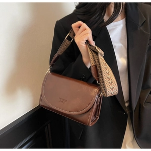 Close-up of brown vintage flap bag with white stitching and woven geometric shoulder strap