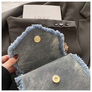 Detail of blue denim crossbody bag with gold magnetic clasp and frayed tassel edges