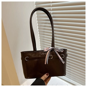 Détail du sac bandoulière en cuir verni marron foncé avec nœud rose et anneau argenté