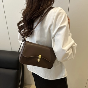 Minimalist chocolate brown crossbody bag with gold twist lock worn by a model