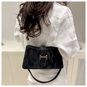 Detail of black pleated baguette bag with gold buckle on shoulder of model in white shirt