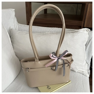 Détail du sac à main en cuir verni beige avec nœud rose sur un canapé blanc