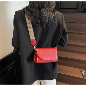 Detail of red leather crossbody bag with vintage ethnic strap on a model's shoulder