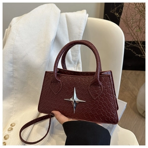 Detail of burgundy crocodile-embossed handbag with silver star ornament and top handle