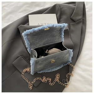 Detail of denim crossbody bag with frayed edges and golden chain, showing inner space