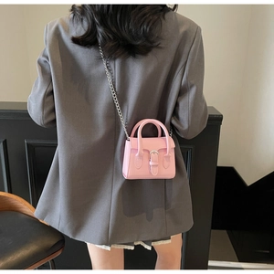 Détail du mini sac carré rose avec chaîne argentée porté par un mannequin en costume gris