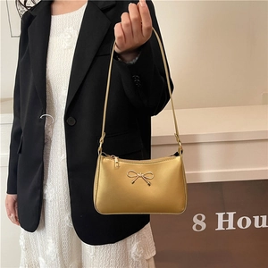 Elegant gold metallic shoulder bag with bow detail held by model in professional suit
