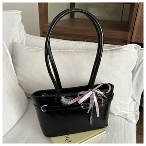 Détail d'un sac à bandoulière noir brillant avec boucle et nœud en soie rose décoratif