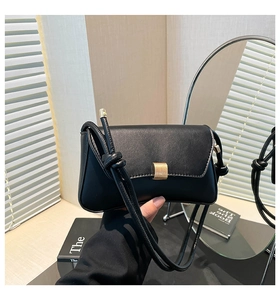 Detail of black underarm bag featuring a gold rectangular buckle and knotted strap accent