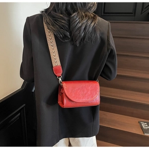 Detail of red leather crossbody bag with ethnic woven strap and golden buckle on model
