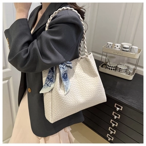 Detail of a creamy white woven tote bag featuring a floral silk scarf and braided handle strap