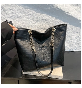 Detail of black crocodile texture tote bag with elegant gold chain handles and leather straps