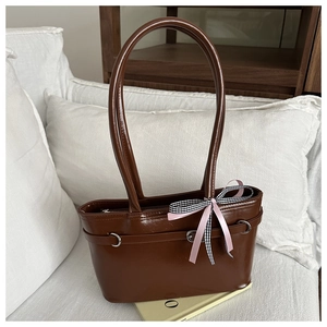 Détail d'un sac à main marron en similicuir avec un nœud rose et à carreaux sur un canapé